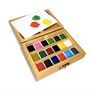 A wooden watercolor paint box with multiple color pans and a white paper palette resting inside, shown on a clean white background.