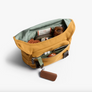 Classic Messenger Bag shown open, filled with travel accessories. Camel bag has a sage green interior, front zip pocket, and key fob.