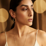 Woman wearing a gold earring and necklace against a warm-toned background