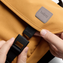 Close-up of a camel Classic Messenger Bag with a person's hands closing the buckle closure on the front flap.