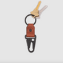 A keychain with a black metal carabiner and key ring, featuring a textured reddish-brown leather tab, shown with two keys on a light gray background.
