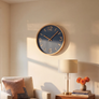 A round wall clock with a blue face and gold-toned frame and hands, mounted on a beige wall in a styled living room with a chair, lamp, and books.